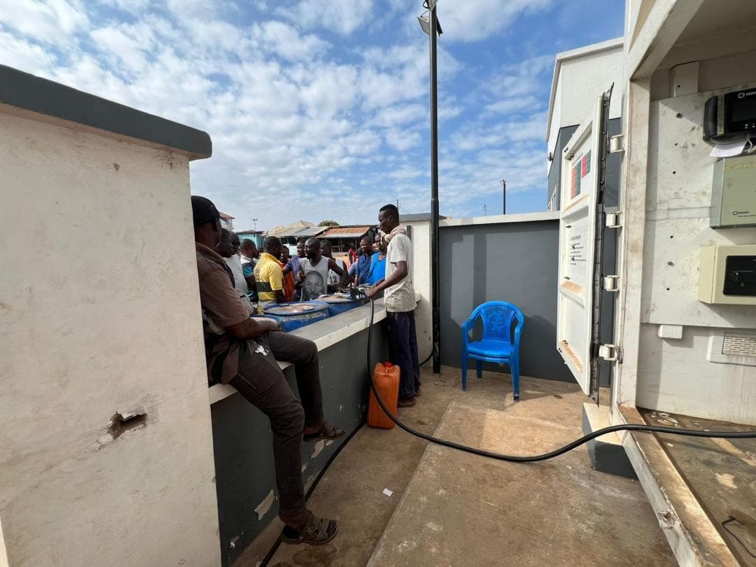 People gathered beside an automated fuel dispenser and yellow fuel containers